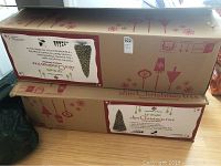 Two cardboard boxes containing a 12' Member's Mark prelit slim Christmas tree; boxes labeled with product details and graphics
