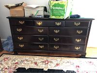 Front view of dresser showing dark wood finish, glass top, brass handles, and closed drawers.