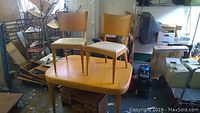 Overall view of mid-century Heywood Wakefield dining table with two chairs placed on top of it in a workshop or storage area.