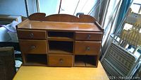Front view of the wooden cupboard showing 5 drawers and 4 compartments, sitting on a table.