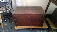 Wooden antique chest showing top and front panels with weathered wood and dovetail corners.