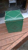 Front view of the green vinyl sewing stool showing square shape, cushioned lid with decorative white piping and diamond stitch design on sides.