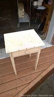 White small table with a single drawer, showing a square top surface, paint worn and discolored.