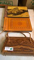 Photo showing two hand-tooled leather albums stacked and one leather purse below them displaying the detailed tooling and overall condition