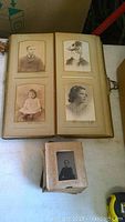 Open large album showing four cartes de visite and cabinet card portraits mounted on thick beige cardstock pages, featuring men, women and children from the late 19th century.
