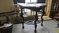 Side view of the wooden demilune style table showing curved top and ornate legs.