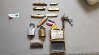Top view of all items laid out including seven pocket knives, two padlocks, assorted keys, and the brass timepiece.