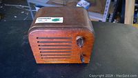 Front and top angled view showing the wood case, front speaker grille with horizontal slats, a wood knob and switch, and worn finish.