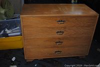 Front view of a four drawer low chest showing metal handles and some surface wear