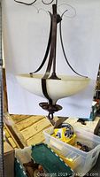 Copper nap pendant chandelier with bowl-shaped frosted glass shade on wooden pallet.