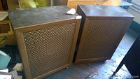 Two large mid-century modern wood cabinet speakers with fabric front grilles and castors, top view shows dust and wear.