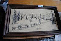 Framed rectangular scrimshaw-style art plaque showing a musher and sled dogs in an Alaskan winter landscape with mountains and pine trees.