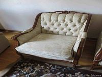 Front view of carved wood frame upholstered chair with tufted backrest and cushion, placed on floral carpet.