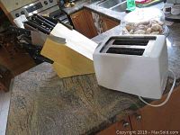 Photo showing the wooden knife block with several black handled knives and white Black and Decker toaster on a kitchen counter