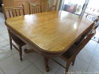 Oak rectangular dining table with six matching chairs shown in a room, visible wood grain and rounded corners on table top.