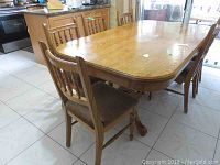 Six oak dining chairs, positioned around a matching oak dining table in a kitchen setting.