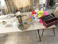 Wide shot showing table with assorted decorative and glass items including trays, faux flowers, glassware, wine box set, and horse-themed vase.