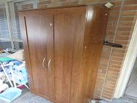 Closed faux wood pantry cabinet showing front with double doors and silver handles, medium brown color, some visible wear.