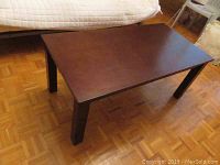 Photo of rectangular dark brown wood coffee table, top view showing smooth surface and four legs.