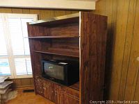 Full view of the faux wood tall cabinet with lower doors and open shelves, placed against a wall with a window nearby. Shows overall size and style.