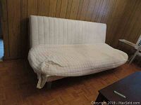 Full view of beige futon showing quilted mattress and backrest on metal and wood frame.