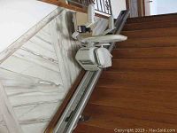 Photo showing the installed Acorn Superglide 130 stair lift on a wooden staircase with metal rail and padded chair.