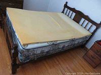 Full view of double bed with wood headboard, mattress with foam topper, and box spring on wood floor.