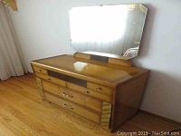 Full view of the Art Deco style wood dresser with attached mirror against a wall.