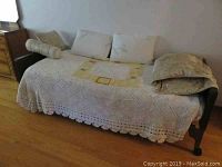 Full view of electric hospital bed covered with a white crocheted cover and multiple pillows laying on top, showing size and overall look.