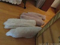 Five faux fur mats laid out on wooden floor, colors include white, cream, and light brown, largest approximately 30x33 inches.