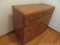 Front view showing the Art Deco style dresser, wooden finish, brass handles, and design details including curved top edge and patterned veneer.