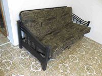 Front and side angle of the futon showing the metal frame and patterned fabric cushions on a tiled floor.