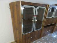 Front view of the tall cabinet showing two glass doors with beveled edges and metal handles, visible faux wood grain finish.