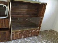 Full view of the tall faux wood cabinet with closed glass doors and lower cabinet doors, showing wood grain finish and condition with scratches.