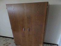 Closed view of the faux wood pantry cabinet showing two doors with silver handles and wood grain finish.