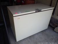 White chest freezer with hinged lid and silver handle, showing some wear and dirt marks.