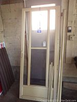 Metal beige storm door leaning against a wall, showing its height, glass, and screen panels.