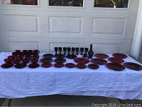Full set of red vintage Avon glass dinnerware arranged on white cloth showing all pieces including plates, bowls, goblets, decanter, candlesticks, and mugs.