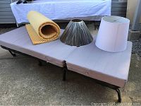 IKEA single size cot with foam mattress cover, yellow foam mattress topper, white and black lamp shades placed on top of cot