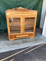 Full front view of the vintage cabinet showing two glass doors, upper drawer with metal handles, and bottom drawer with brass handle.