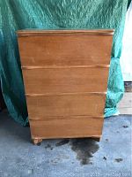 Full front view of a vintage tallboy dresser showing four drawers with recessed wooden pull handles, finished in medium wood tone.