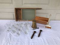 All items arranged on white tablecloth including glasses, bread cutter, washboard, cowbell, spikes, and can opener