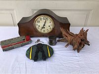 Overview of mantel clock, petrified wood, Hoosier train engine, metal cup, and Battlestar Galactica Cylon ship toy on white cloth.