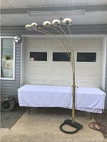 Full view of the five-arm brass arc floor lamp against garage door.
