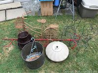 Wide shot showing all items in set including bicycle plant stand, brown ceramic cup pot with saucers, white umbrella base, copper bin, metal butterfly and heart plant stands, red metal frame in background.