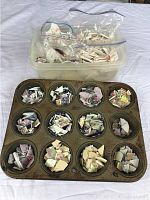 Broken china pieces sorted by type and color placed inside the cups of a Bakers Secret metal muffin pan.