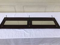Vintage wooden coat rack laid flat on a white cloth with two bevel-edged rectangular mirrors and six metal double hooks mounted.