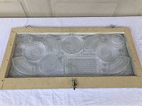 Front view of vintage wooden window frame with embedded pressed glass plates, showing rectangular shape and cream paint.