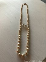 Full view of 18-inch pearl necklace with matching pearl stud earrings laid flat