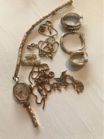 All components displayed on white surface: watch, bracelets, chains, earrings and charms
